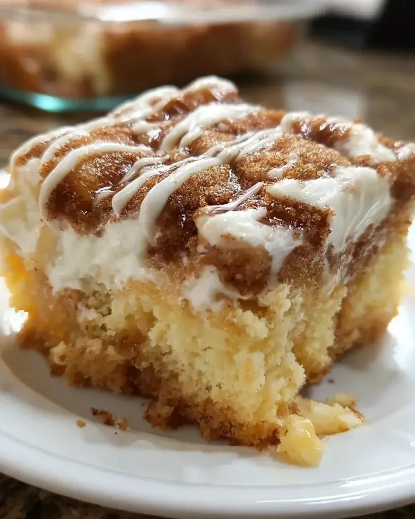 Sliced cinnamon roll poke cake topped with cream and cinnamon icing