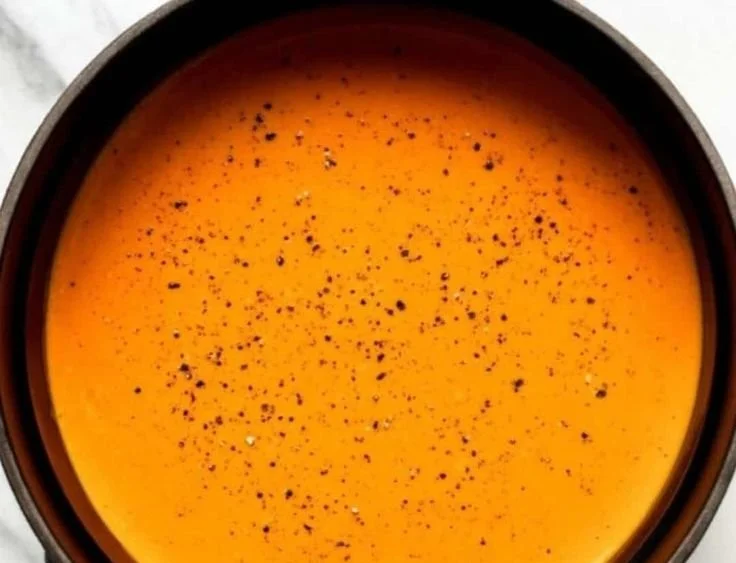 Bowl of creamy roasted red pepper soup garnished with herbs