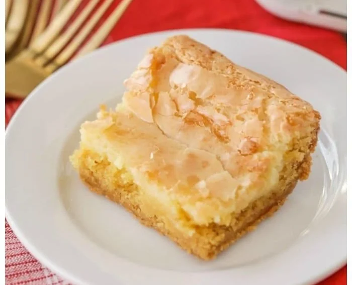 Delicious slice of gooey butter cake topped with powdered sugar on a plate