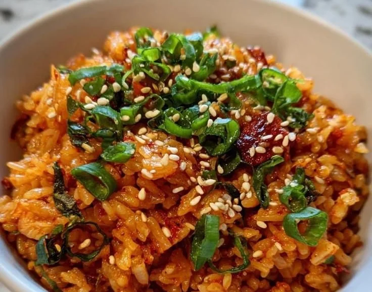 A bowl of vibrant kimchi fried rice garnished with green onions and sesame seeds.