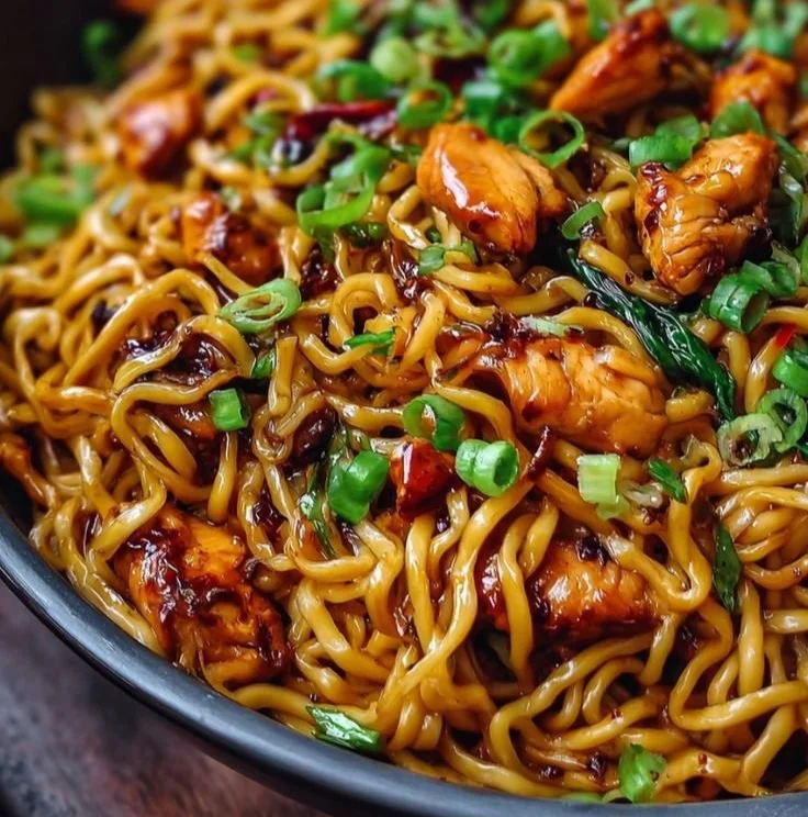 Plate of sticky garlic chicken noodles garnished with green onions