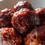 Plate of sweet-and-savory grape jelly meatballs garnished with herbs.