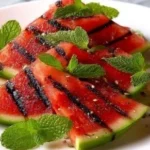 Grilled watermelon with mint served on a plate, garnished for a summer treat.