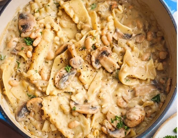 A bowl of mushroom and white bean pasta garnished with fresh herbs.
