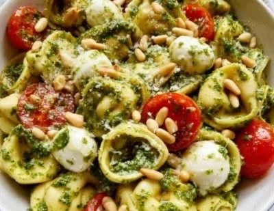 Bowl of vibrant Pesto Tortellini Salad with fresh vegetables and dressing.