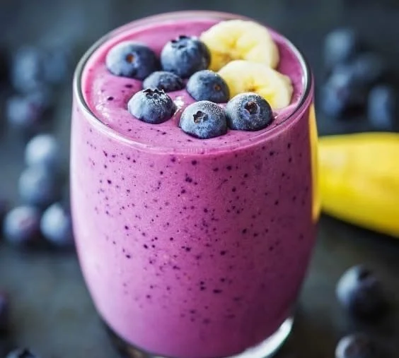 Healthy blueberry banana smoothie in a glass with fresh berries and banana slices.