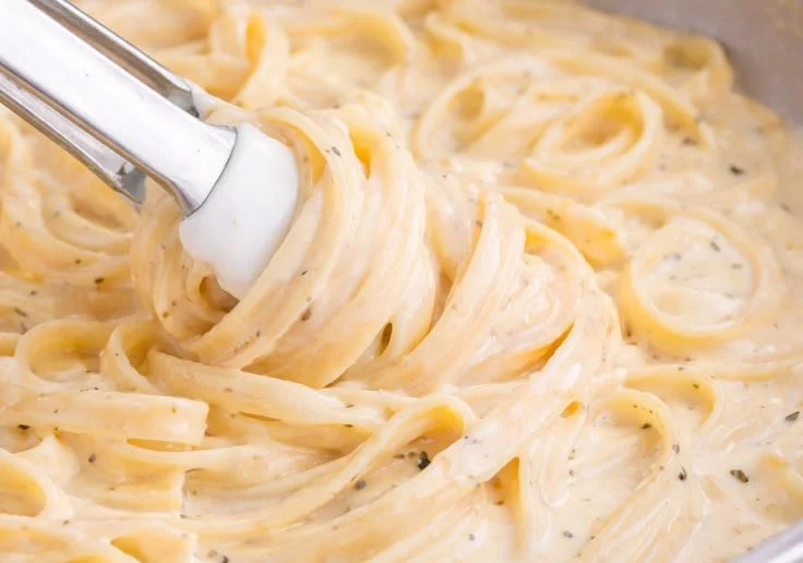 Bowl of creamy homemade Alfredo Sauce with fresh herbs and Parmesan cheese.