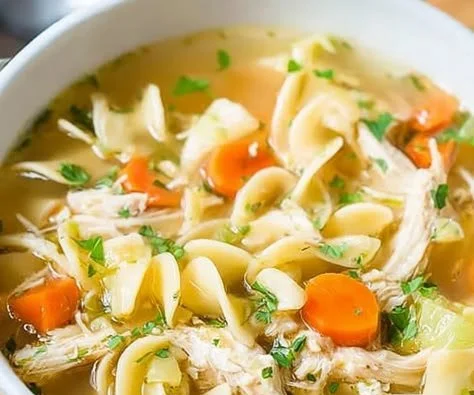 A bowl of homestyle chicken noodle soup with fresh vegetables and herbs.
