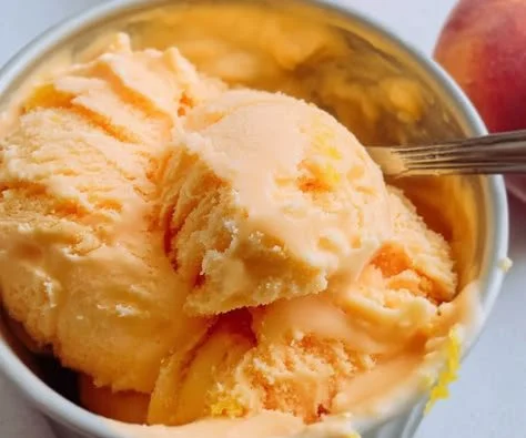 A bowl of refreshing peach sherbert with fresh peaches on the side.